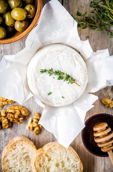 Whole Camembert cheese with walnuts, olives, honey and baguette — Stock Photo, Image