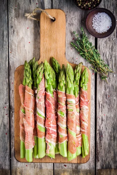 Fresh organic asparagus wrapped in Parma ham on a cutting board — Stock Photo, Image