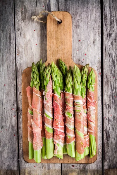 Fresh organic asparagus wrapped in prosciutto on a cutting board — Stock Photo, Image