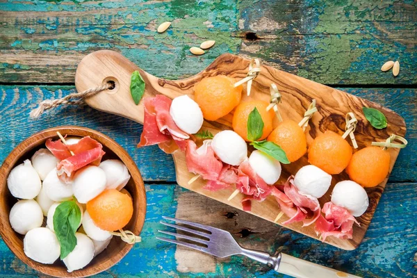 Mozzarella and prosciutto with melon canapes with basil on a cutting board — Stock Photo, Image