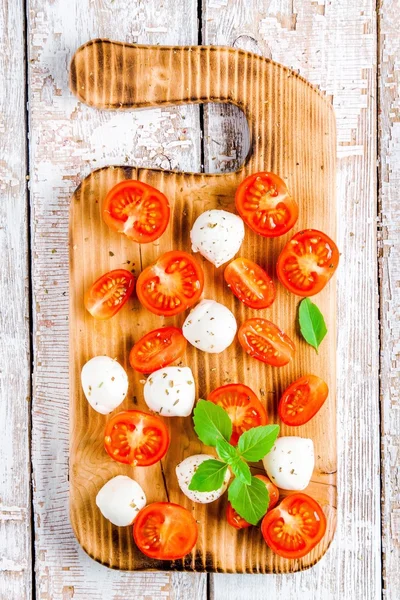 Mussarela, tomate cereja e manjericão na velha tábua de corte — Fotografia de Stock