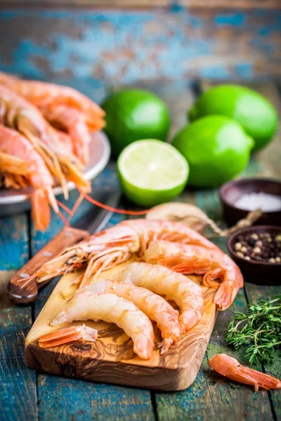 Crevettes crues pelées sur une planche à découper en bois avec sel, poivre, citron vert — Photo