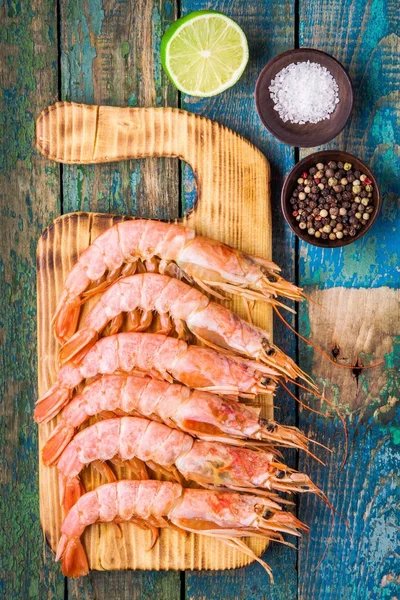Fresh raw shrimps on a wooden cutting board with salt, pepper, lime — Stock Photo, Image