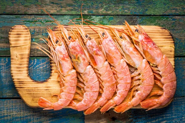 Langostinos frescos crudos en una tabla de cortar de madera — Foto de Stock