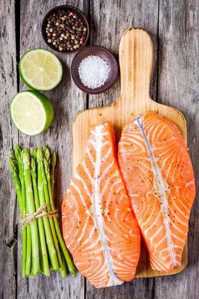 Filete de salmón fresco en una tabla de cortar de madera con espárragos — Foto de Stock