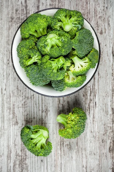 Fresh raw organic broccoli in bowl on a wooden background — Stock Photo, Image