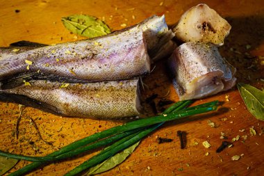 Tahta bir masada taze soğan ve baharatla taze balık parçaları..