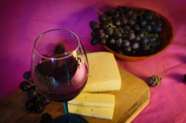 Mor arka planda peynirli ve üzümlü bir kadeh kırmızı şarap.