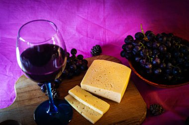 Mor arka planda peynirli ve üzümlü bir kadeh kırmızı şarap.
