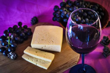 Mor arka planda peynirli ve üzümlü bir kadeh kırmızı şarap.