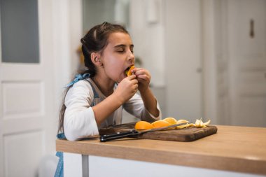 Küçük kız pozitif duygularla kameraya bakarak bir portakal yiyor. Mandarin ve bebek. Çocuklar için yiyecek. Meyveler ve meyveler.