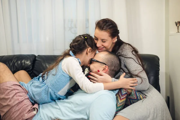 Babam kanepede aileye katılır ve herkesi gıdıklamaya başlar. Genç kaygısız ebeveynler ve küçük kız gülüyor. Evde sarılıp oynuyorlar. Kanepede eğlenceli bir oyun oynuyorlar..