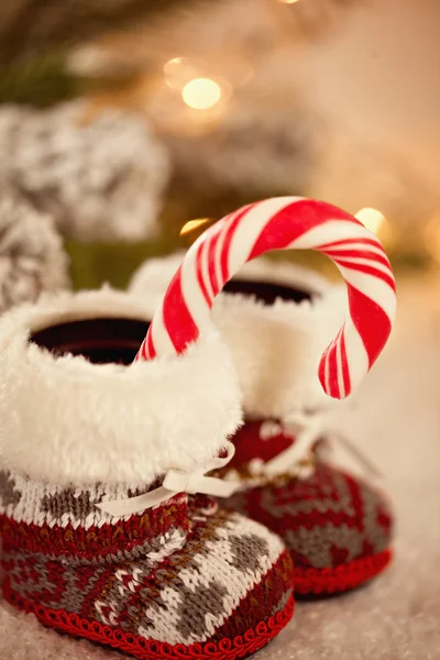 Zapatillas de bebé cerca con bastón de caramelo sobre fondo cubierto de nieve — Foto de Stock