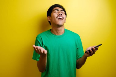 Çekici Asyalı genç adam telefonunda mesajlaşırken okuyor. Kötü haber, sarı arka planda ağlayan üzgün surat.
