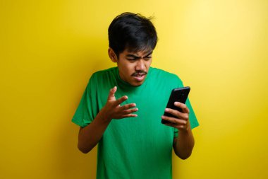 Çekici Asyalı genç adam telefonunda mesajlaşırken okuyor. Kötü haber, sarı arka planda ağlayan üzgün surat.