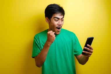Çekici genç Asyalı adamın telefonunda iyi haberler var. Sarı arka plana karşı gülen mutlu bir gülücük.