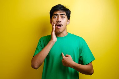 Asyalı genç adam kendini işaret ederek sarı arka planda izole edilmiş şok tepkisi verdi.