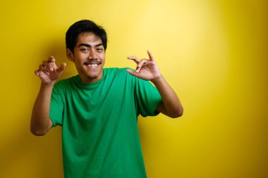 Yeşil tişörtlü Asyalı adam gülümsüyor ve mutlu bir şekilde dans ediyor. İyi haberi kutluyor. Zafer kazanıyor.