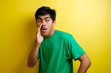 Yeşil tişörtlü genç Asyalı bir adamın portresi. Gizlice konuşuyor. Sarı arka plandaki birine sırrını anlatıyor.