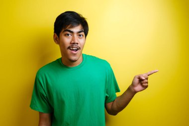 Gülümseyen yakışıklı Asyalı adam sarı arka planda izole edilmiş boş bir eli işaret ediyor.