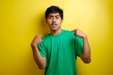 Asyalı genç adam kendini işaret ederek sarı arka planda izole edilmiş şok tepkisi verdi.