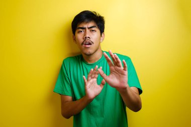 Yeşil tişörtlü genç Asyalı adam sarı arka plana karşı jest yapıyor.