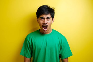 Asyalı bir adamın sarı arka planda kızgın ve öfkeli bir yüz ifadesi..