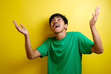 Zaferi kutlayan Asyalı genç bir adamın portresi, kazanan bir jest gülümsemesi ve yukarıdan bir şeyi fotokopi alanı konseptiyle selamlama.