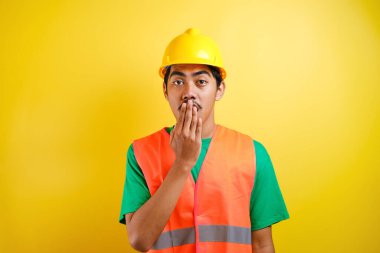 Kask takan Asyalı işçi, elleri sarı arka planda ağzını kapatırken haberi duyunca şok olmuş gibi görünüyor.
