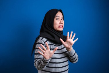 Asian muslim student girl making stop gesture, against blue background. stop to do bullying to her