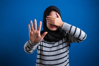 Asian muslim student girl making stop gesture, against blue background. stop to do bullying to her