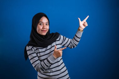 Portrait of Asian young happy asian muslim student girl smiling and pointing to presenting something on her side, with copy space