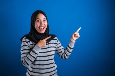 Portrait of Asian young happy asian muslim student girl smiling and pointing to presenting something on her side, with copy space