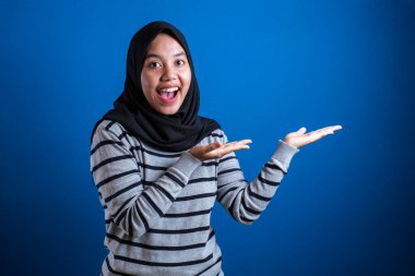 Portrait of Asian young happy asian muslim student girl smiling and pointing to presenting something on her side, with copy space