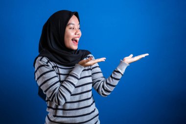 Portrait of Asian young happy asian muslim student girl smiling and pointing to presenting something on her side, with copy space