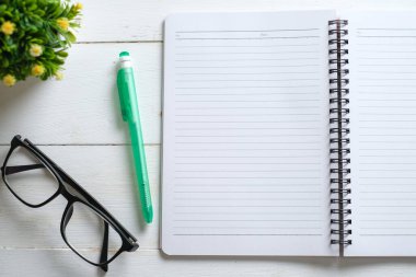 Not defteri, gözlük, kalem ve dekoratif bitkilerle dolu beyaz ahşap bir masa. Kopyalama alanı olan üst görünüm, düz yatay.