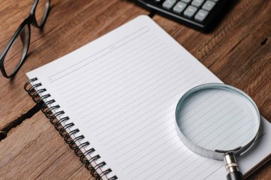 Not defteri, gözlük, büyüteç, kalem ve dekoratif bitkilerle dolu ahşap masa. Kopyalama alanı olan üst görünüm, düz yatay.