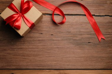 Kırmızı kurdeleli hediye kutusunun seçici odak noktası ve kırsal ahşap masa üzerinde aşk şekilli kağıt, üst görünüm düz.