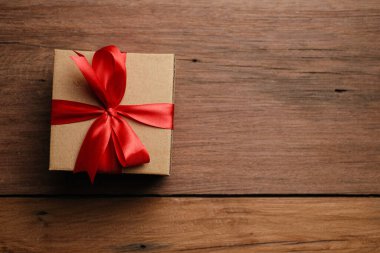 Kırmızı kurdeleli hediye kutusunun seçici odak noktası ve kırsal ahşap masa üzerinde aşk şekilli kağıt, üst görünüm düz.