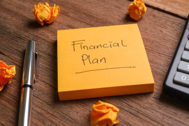 Tahta bir tahtanın yanında kalem ve hesap makinesiyle Finansal Planla yazılmış bir not.