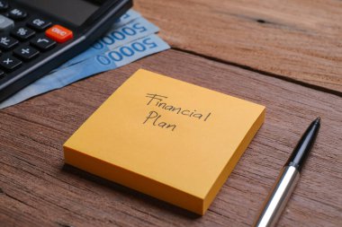 Tahta bir tahtanın yanında kalem ve hesap makinesiyle Finansal Planla yazılmış bir not.