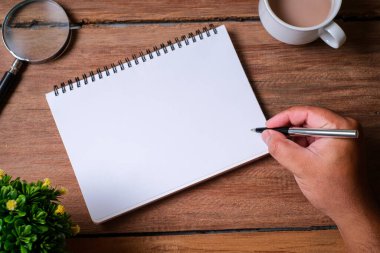 Tahta masa, defter, büyüteç, kalem, dekoratif bitkiler. Kopyalama alanı olan üst görünüm, düz yatay.