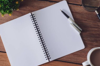Tahta masa, defter, büyüteç, kalem, dekoratif bitkiler. Kopyalama alanı olan üst görünüm, düz yatay.