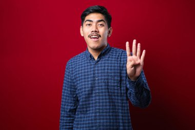 Yakışıklı, gündelik giysiler giymiş dört numarayı gösterip işaret eden kırmızı arka planda mutlu ve kendinden emin genç bir adam.