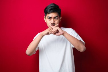 Bıyıklı, beyaz tişörtlü, Asyalı genç adam. Reddedilmiş yüz ifadesi. Kırmızı arkaplanda negatif işaret veriyor.