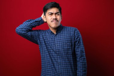 Bıyıklı, normal gömlekli genç ve yakışıklı bir adam kırmızı arka planda dikiliyor. Soruyu merak ediyor. Şüpheyle kararsız, kafa kafaya düşünerek. Düşünceli kavram.