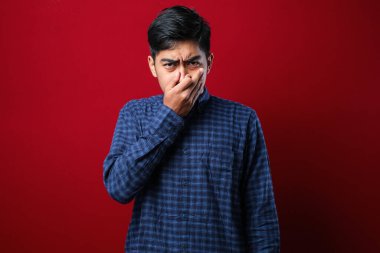 Genç Asyalı bir adam kırmızı arka plan üzerine sıradan bir tişört giyerek pis ve iğrenç bir koku alıyor. Dayanılmaz bir koku. Nefesini burnunda tutuyor. Kötü kokuyor.