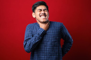 Genç yakışıklı Asyalı bir adam kırmızı arka planda günlük gömlekler giyip bağırıyor ve boğuluyor çünkü acı verici bir boğulma var. Sağlık problemi. Boğulma ve intihar konsepti.