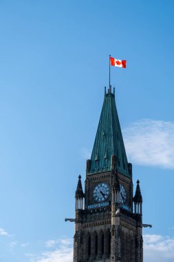 Kanada, Ottawa 'daki Parliament Hill' deki Barış Kulesi 'nin üst kısmı bulutlu mavi gökyüzüne karşı alçak bir açıyla. Saat kulesinin tepesinde rüzgarda dalgalanan Kanada bayrağı.