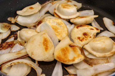 Close-up of pierogi and onions being cooked on a stovetop fry pan. clipart
